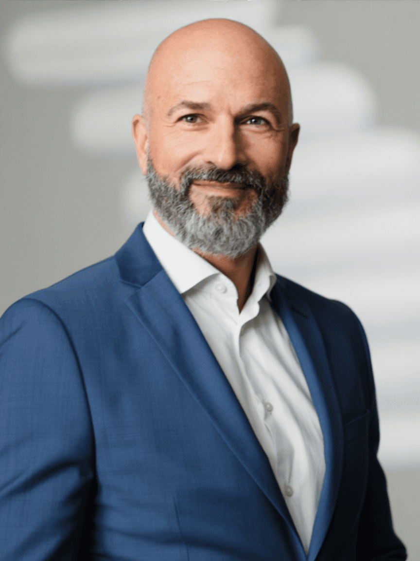 Smiling bald man with a salt-and-pepper beard wearing a blue suit and white shirt.